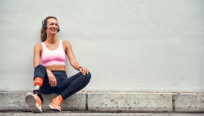 simply-happy-young-smiling-woman-with-leg-prosthesis-sports-clothing-headphones-listening