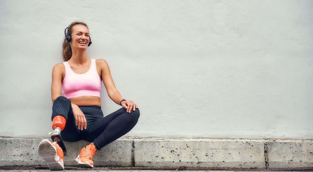 simply-happy-young-smiling-woman-with-leg-prosthesis-sports-clothing-headphones-listening